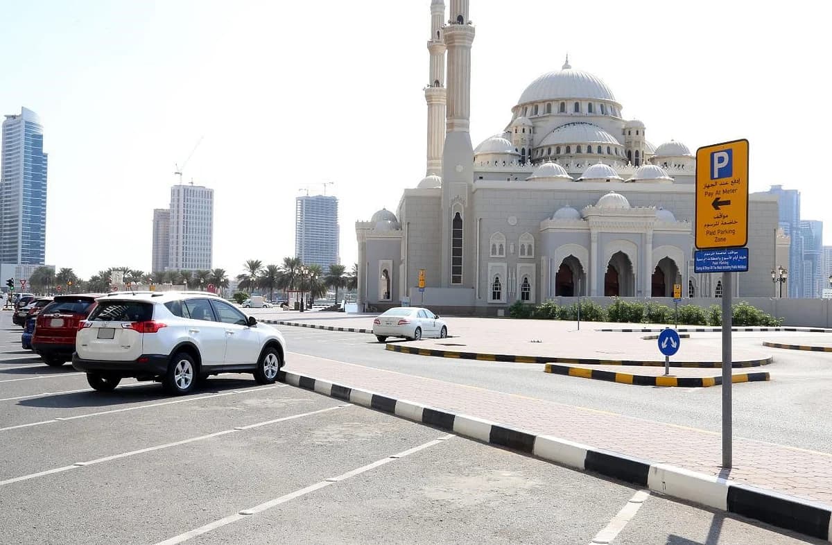 Sharjah City skyline with parking signs indicating new hours.