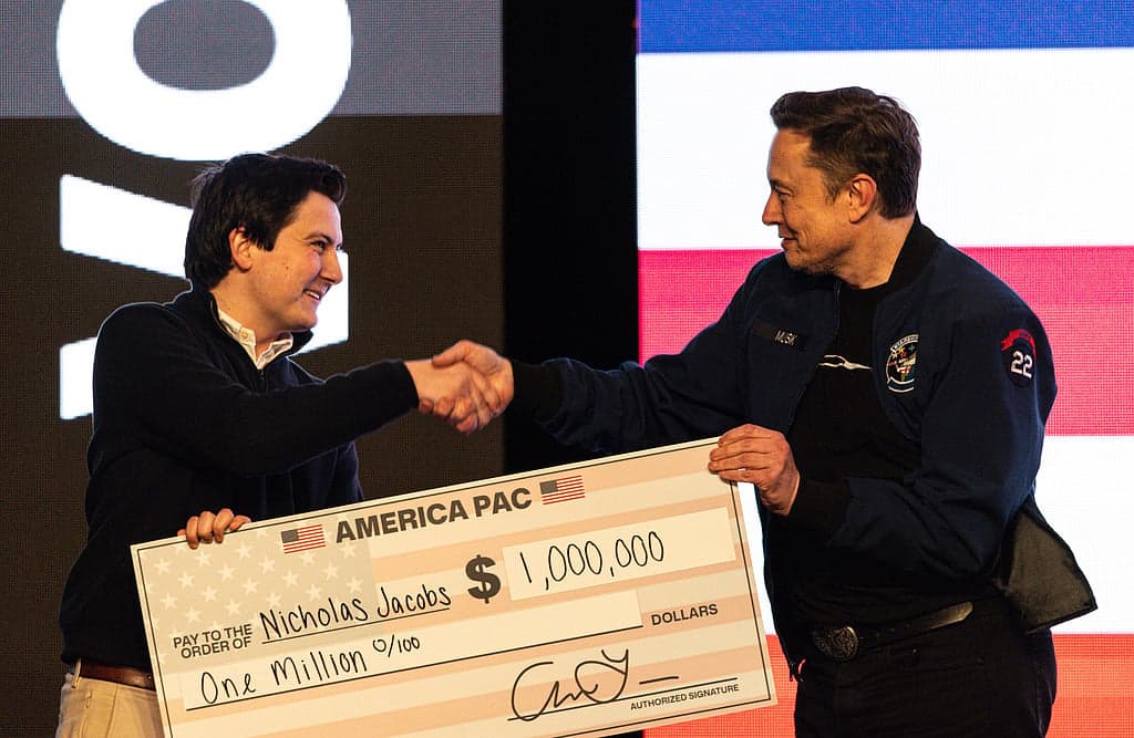Elon Musk speaking at a public event with a backdrop of election-related imagery.