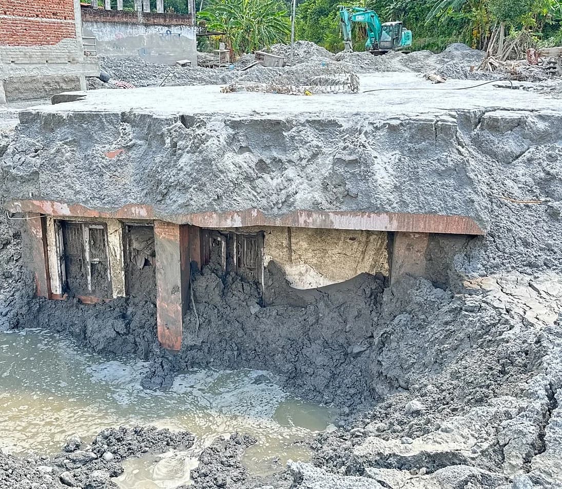 An excavator digging out a flood-buried home in Nepal, highlighting the impact on expatriates.